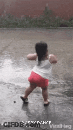 A Little Girl Is Dancing In The Rain In A Puddle Of Water . GIF