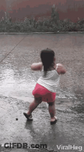 A Little Girl Is Dancing In The Rain On A Wet Sidewalk . GIF