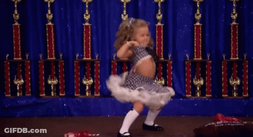 A Little Girl Is Dancing On A Stage With Trophies Behind Her GIF