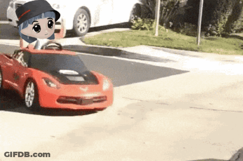 A Little Girl Is Driving A Red Toy Car On The Street GIF