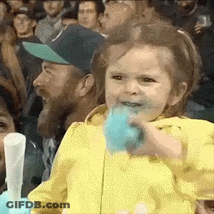 A Little Girl Is Eating Cotton Candy While Sitting In A Crowd . GIF