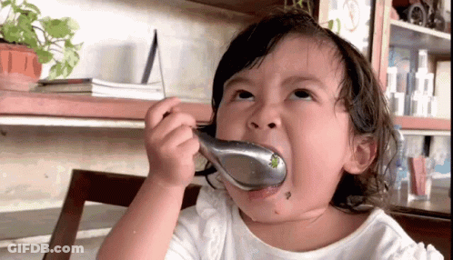 A Little Girl Is Eating Something With A Spoon In Her Mouth GIF