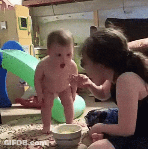 A Little Girl Is Feeding A Baby From A Bowl On The Floor GIF