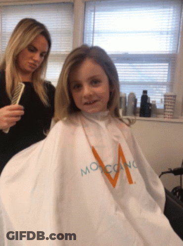 A Little Girl Is Getting Her Hair Cut By A Woman Wearing A White Cape That Says Moroccano GIF