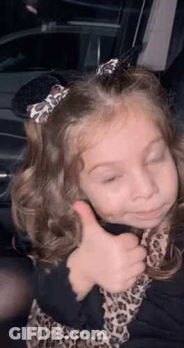 A Little Girl Is Giving A Thumbs Up While Sitting In A Car . GIF