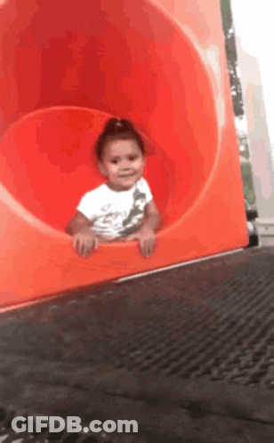A Little Girl Is Going Down A Red Slide GIF