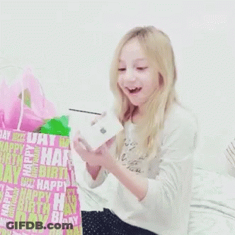 A Little Girl Is Holding A Box In Front Of A Birthday Bag That Says Happy Birthday GIF