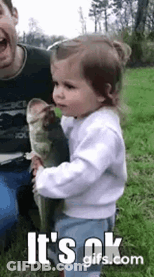 A Little Girl Is Holding A Large Fish In Her Arms . GIF
