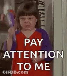 A Little Girl Is Holding A Toy And Making A Funny Face And Says `` Pay Attention To Me '' . GIF