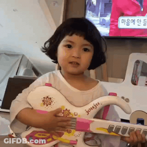 A Little Girl Is Holding A Toy Guitar In Her Hands . GIF