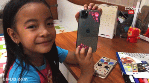 A Little Girl Is Holding An Apple Iphone In Her Hand GIF