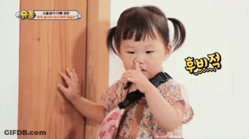 A Little Girl Is Holding Her Nose While Standing In Front Of A Wooden Door . GIF