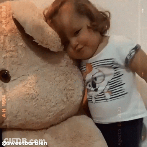 A Little Girl Is Hugging A Giant Teddy Bear GIF