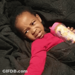 A Little Girl Is Laying On A Bed Holding A Pink Bottle . GIF