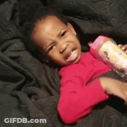A Little Girl Is Laying On A Bed With A Bottle Of Milk In Her Hand . GIF