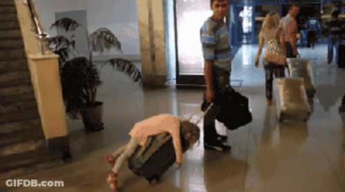 A Little Girl Is Laying On A Suitcase While A Man Pushes A Suitcase GIF