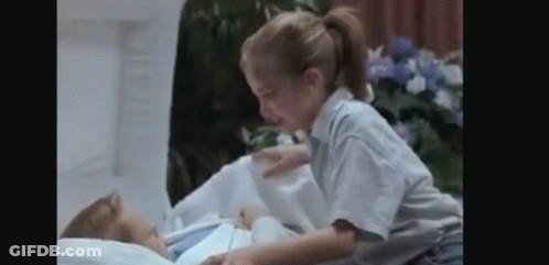A Little Girl Is Laying On Top Of A Corpse In A Hospital Bed . GIF