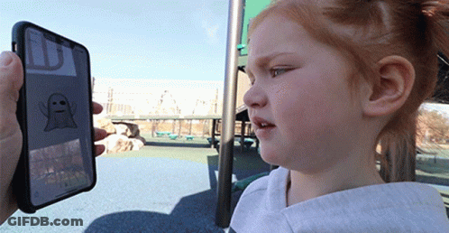 A Little Girl Is Looking At A Phone With A Ghost On The Screen GIF