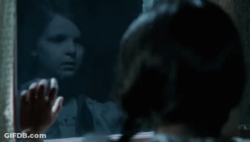 A Little Girl Is Looking Out A Window At Her Reflection In The Mirror . GIF