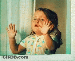 A Little Girl Is Looking Out Of A Window And Waving Her Hand GIF
