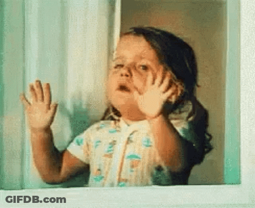 A Little Girl Is Looking Out Of A Window And Waving Her Hands . GIF