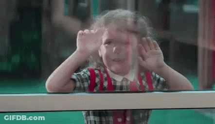 A Little Girl Is Looking Out Of A Window . GIF