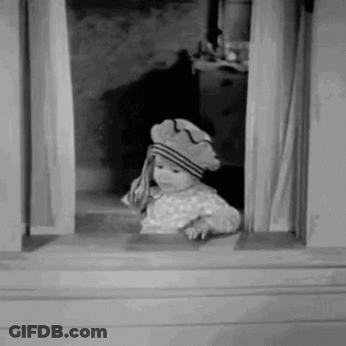 A Little Girl Is Looking Out Of A Window Wearing A Hat . GIF