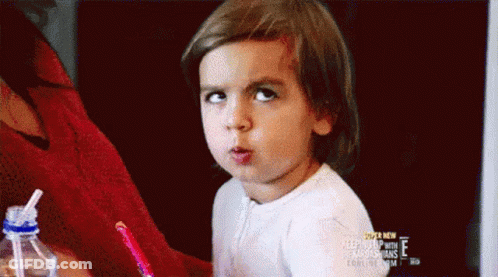 A Little Girl Is Making A Funny Face While Sitting At A Table . GIF