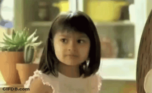 A Little Girl Is Making A Funny Face While Sitting In Front Of Potted Plants . GIF
