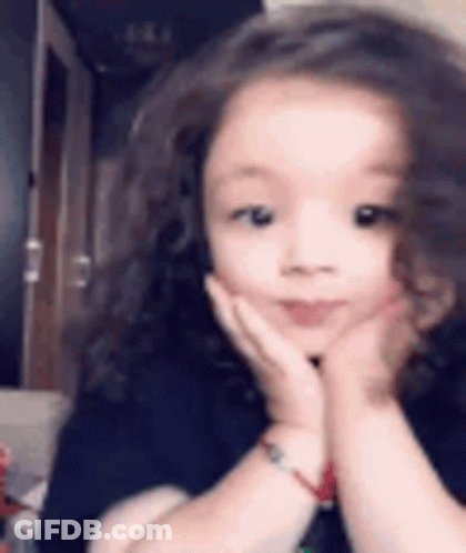 A Little Girl Is Making A Funny Face With Her Hands On Her Face . GIF