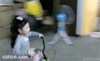 A Little Girl Is Riding A Bike With A Fan In The Background GIF