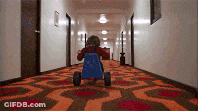 A Little Girl Is Riding A Blue Go Kart Down A Hallway . GIF