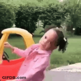 A Little Girl Is Riding In A Toy Car . GIF