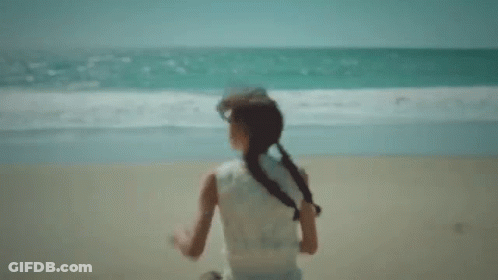 A Little Girl Is Running On A Beach Near The Ocean . GIF