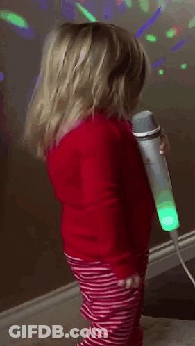 A Little Girl Is Singing Into A Microphone In A Room GIF