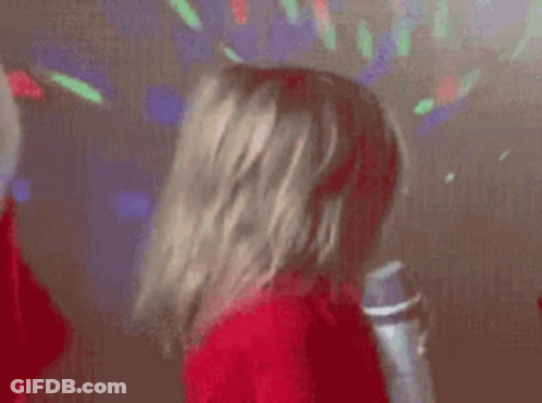 A Little Girl Is Singing Into A Microphone While Wearing A Red Sweater . GIF