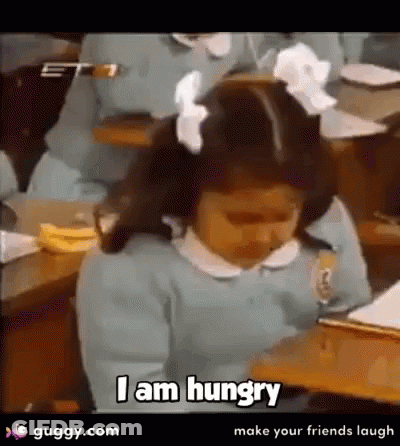 A Little Girl Is Sitting At A Desk Saying I Am Hungry . GIF