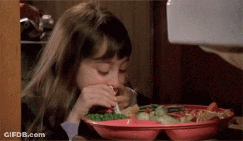 A Little Girl Is Sitting At A Table Eating A Plate Of Food With A Fork . GIF