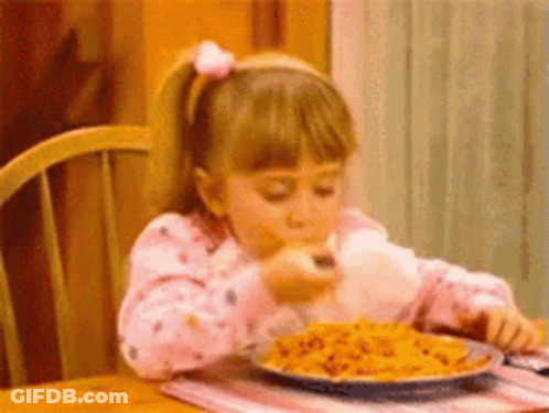 A Little Girl Is Sitting At A Table Eating A Plate Of Pasta . GIF