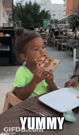 A Little Girl Is Sitting At A Table Eating A Slice Of Pizza . GIF