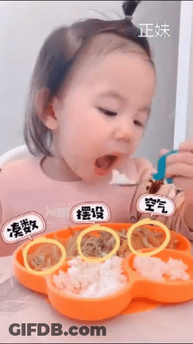 A Little Girl Is Sitting At A Table Eating Food From A Flower Shaped Plate GIF