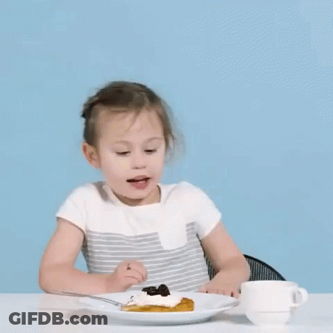 A Little Girl Is Sitting At A Table With A Plate Of Food . GIF
