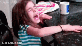 A Little Girl Is Sitting At A Table With Her Arms Outstretched And Screaming . GIF