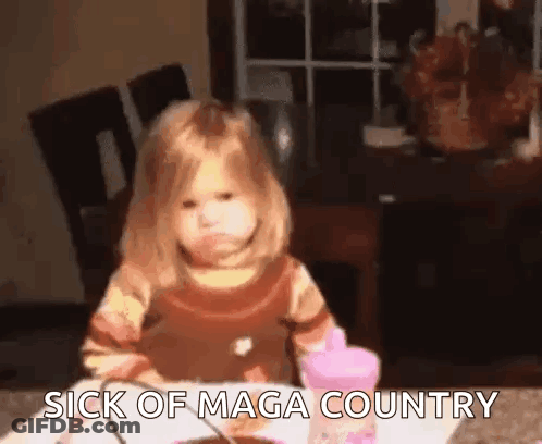 A Little Girl Is Sitting At A Table With The Words `` Sick Of Maga Country '' Written On The Table . GIF