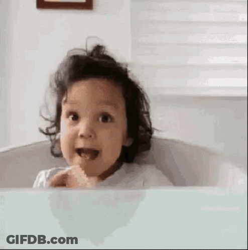 A Little Girl Is Sitting In A Bathtub With Her Mouth Open And Eating Something . GIF