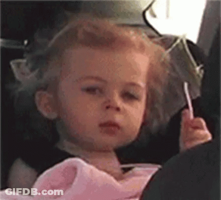 A Little Girl Is Sitting In A Car Seat Holding A Lollipop GIF