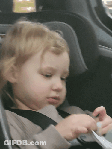 A Little Girl Is Sitting In A Car Seat With A Seat Belt On GIF