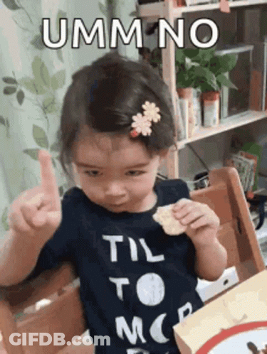 A Little Girl Is Sitting In A Chair Eating A Snack And Giving A Thumbs Up Sign . GIF