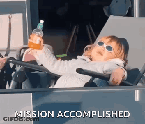A Little Girl Is Sitting In A Chair Holding A Bottle Of Orange Juice And The Words Mission Accomplished Behind Her GIF