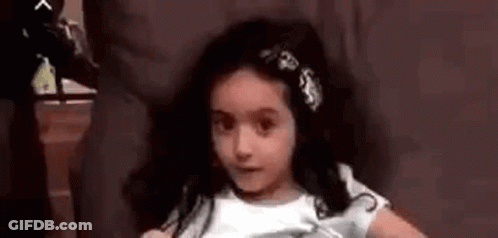 A Little Girl Is Sitting In A Chair With A Flower In Her Hair And Making A Funny Face . GIF